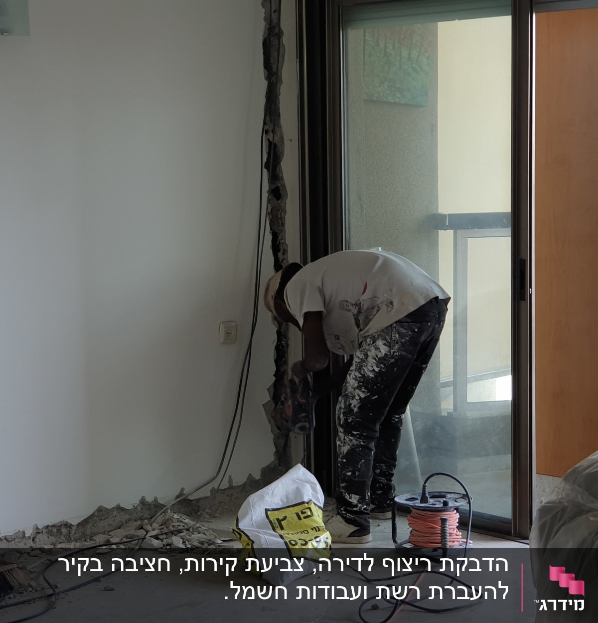 עובד קודח בקיר עם מקדחה חשמלית, כבלים על הרצפה